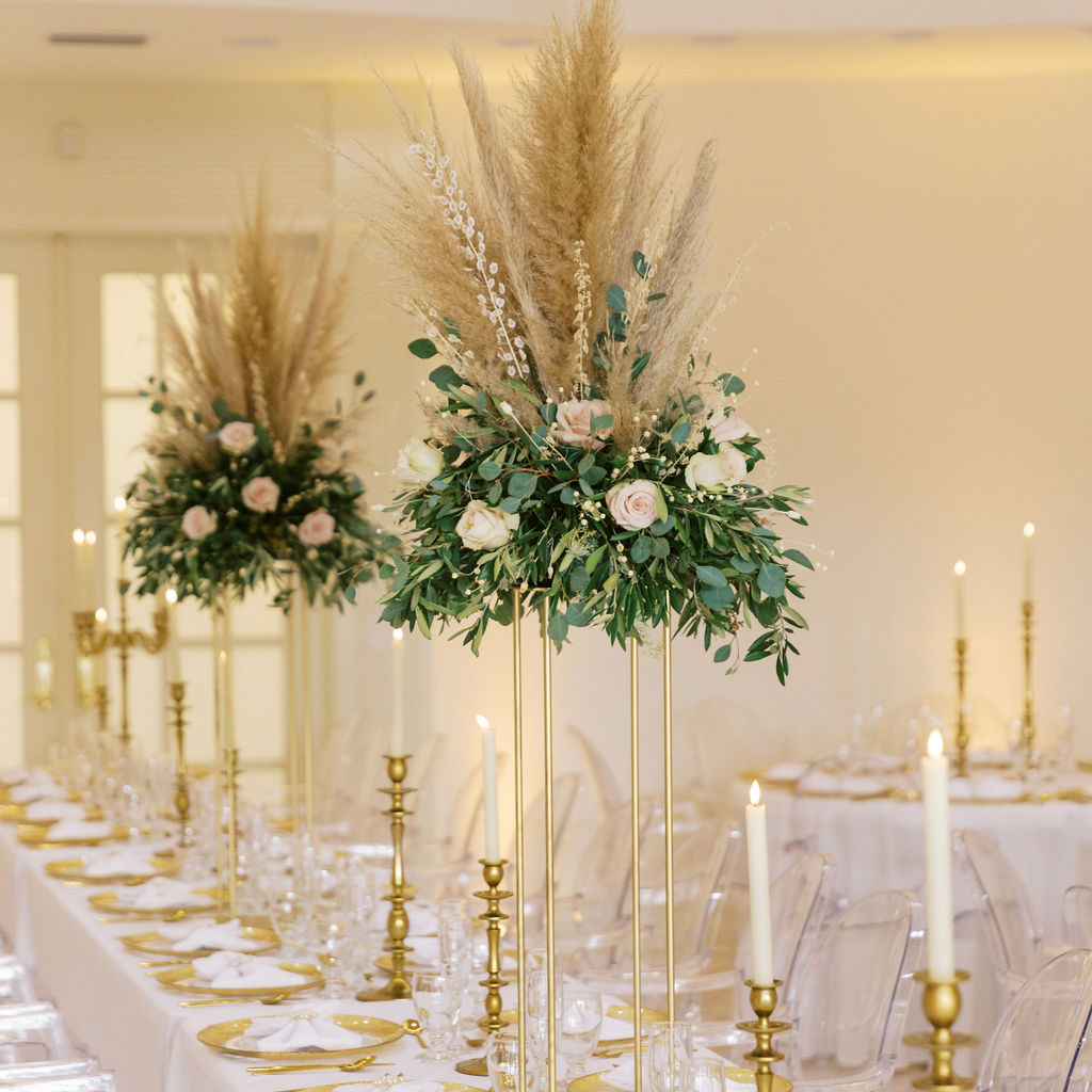 A smiling bride on a beach at dusk is holding a bouquet of white roses to match her white wedding dress and vel, and hugging a young girl of about 8 years old who is also wearing a long white dress and has flowers in her hair.