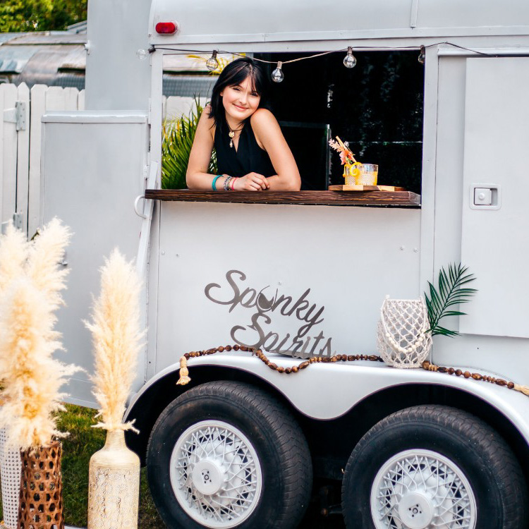 image of young woman leaning on the counter of a white mobile bar trailer with a pineapple and other decorations